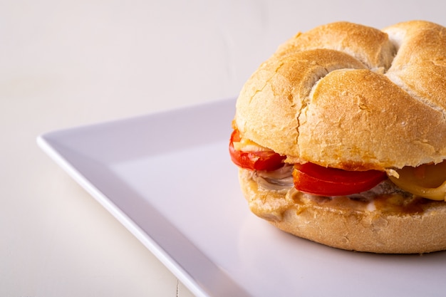 Hambúrguer caseiro único Vienna Kaiser pão com frango, tomate, mostarda, maionese em prato quadrado branco, close-up