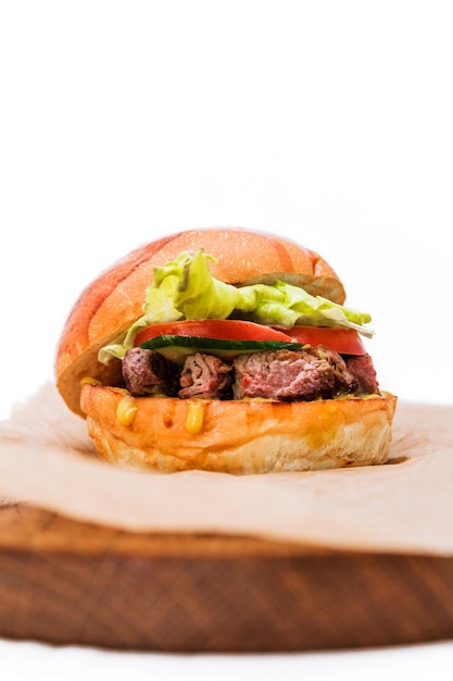 Hambúrguer com carne assada de carne macia tomate pepino alface e molho de queijo em uma placa de madeira em um fundo branco