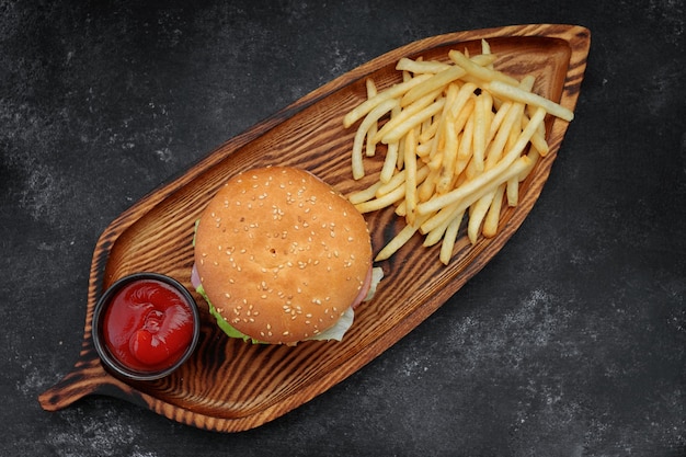 Hambúrguer com carne, tomate e queijo, batata frita e molho em um plano de fundo preto vista superior