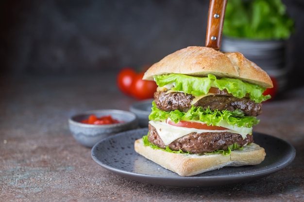 Hambúrguer com hambúrguer de carne bovina e legumes frescos em fundo escuro. saborosa comida rápida.