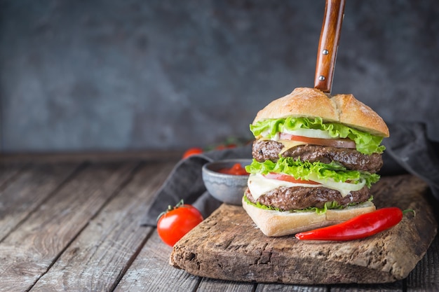 Hambúrguer com hambúrguer de carne bovina e legumes frescos em fundo escuro. Saborosa comida rápida.