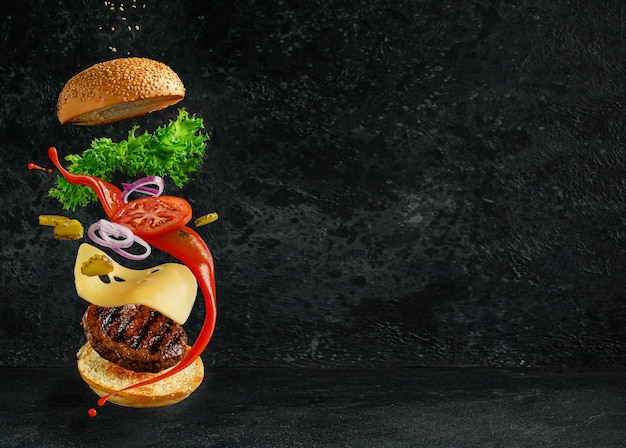 Hambúrguer com ingredientes flutuantes no escuro. Conceito de natureza morta criativa e propaganda