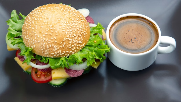 Hambúrguer com legumes, salsicha e café numa superfície cinzenta. Fast food e café da manhã. Calorias e dieta.