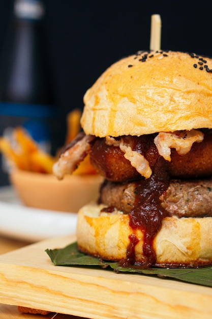 Foto hambúrguer com molho barbecue, cerveja e batata frita.