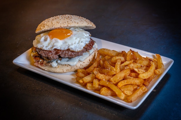 Hambúrguer com ovo frito e batata frita em um fundo preto, em um prato branco