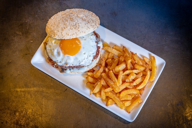 Hambúrguer com ovo frito e batata frita em um fundo preto, em um