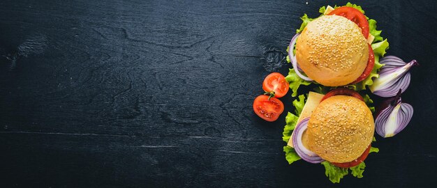 Hambúrguer com queijo carne tomate e cebola e ervas no fundo de madeira vista superior Espaço livre