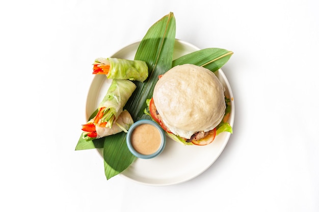 Hambúrguer com rolinhos primavera de pães cozidos no vapor Bao e molho de gergelim no prato isolado