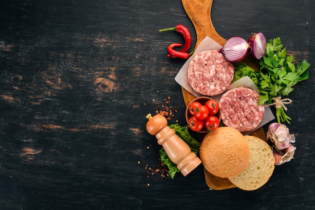 Hambúrguer cru Cozinhar um hambúrguer com carne Em um fundo preto de madeira Vista superior Espaço para cópia grátis