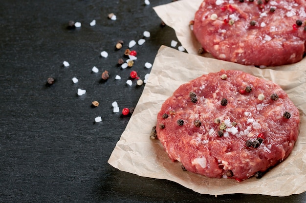 Hambúrguer de bife fresco caseiro picado com especiarias, em uma mesa de ardósia preta, copie o espaço