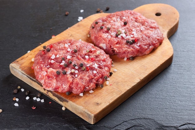 Hambúrguer de bife fresco caseiro picado com especiarias, em uma tábua de cortar na mesa de ardósia preta, cópia espaço, vista de cima