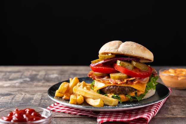 Hambúrguer de carne com queijo, bacon e batata frita na mesa de madeira