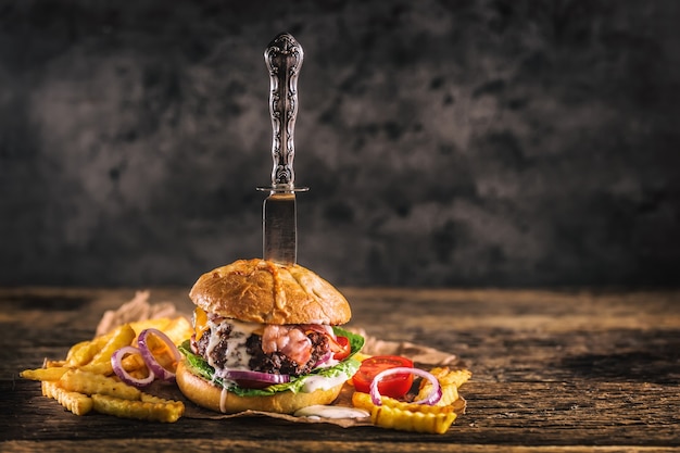 Hambúrguer de carne feito em casa de close-up com faca e batatas fritas na mesa de madeira.