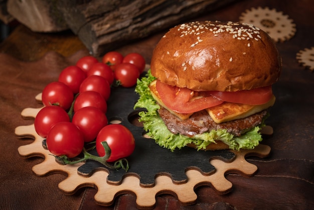 Foto hambúrguer de carne fresca com um ramo de tomate cereja fresco servido em uma peça decorativa de madeira com um mecanismo simples