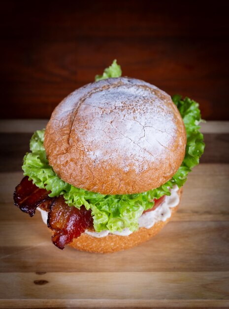 Foto hambúrguer de frango com bacon, alface, tomate, queijo cheddar e cebola servido em uma tábua de madeira preta. hambúrger de frango artesanal feito à mão