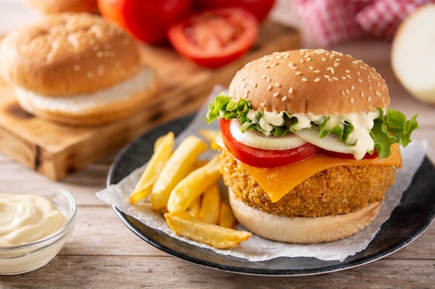 Hambúrguer de frango crocante com queijo e batata frita na mesa de madeira