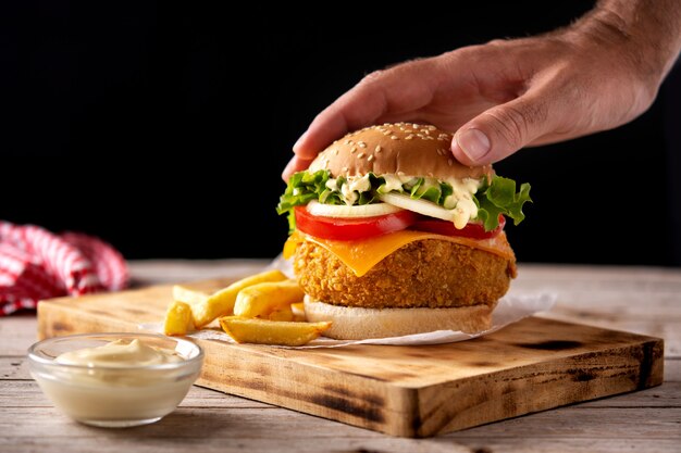 Hambúrguer de frango crocante com queijo e batata frita na mesa de madeira