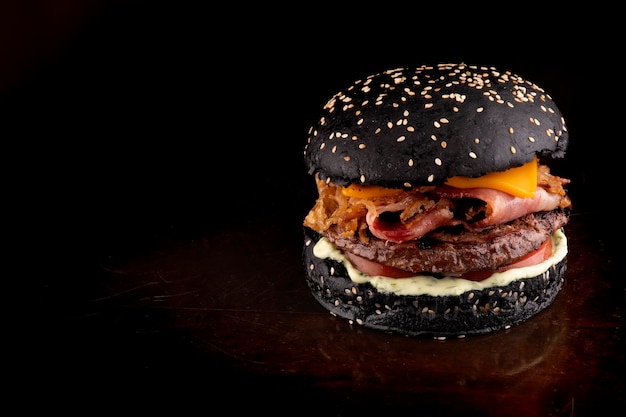 Hambúrguer de gordura com tema de halloween engraçado pão preto crocante bacon e fatias de cebola com gergelim na mesa de madeira vista de ângulo no canto