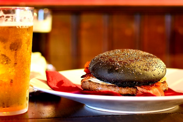 Foto hambúrguer de pão preto com cerveja em uma mesa de madeira