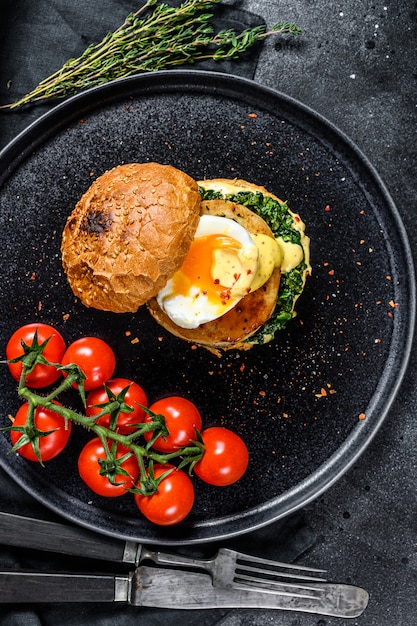 Hambúrguer de peixe caseiro com filé de bacalhau, ovo e espinafre em um bolo de brioche. superfície preta. vista do topo