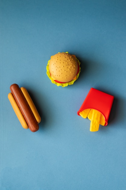 Hambúrguer de plástico, salada, tomate, fritar batatas com um cachorro-quente em um fundo azul