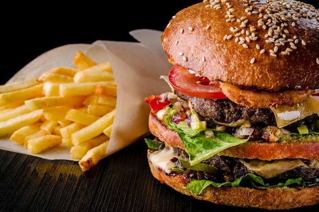 Hambúrguer de queijo com carne grelhada, queijo, tomate e batatas na superfície de madeira escura. Modelo de fast food. Foto real. Ideal para propaganda. Fechar-se. Natureza morta hambúrguer e batatas fritas