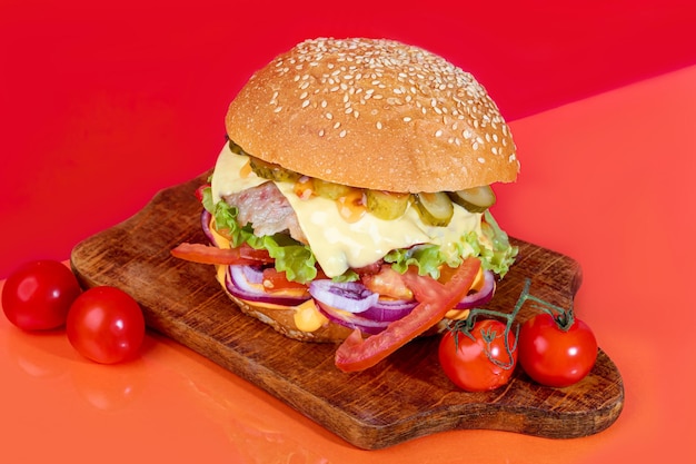 Hambúrguer delicioso a bordo com tomates de costeleta e pepino de queijo e alface Em um fundo vermelho Fast food