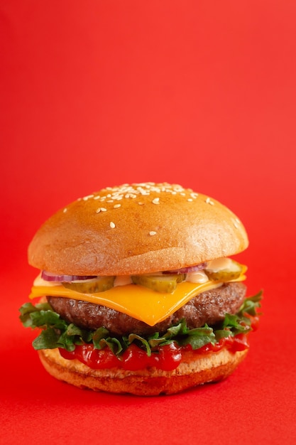 Hambúrguer delicioso com carne e queijo cheddar em um fundo vermelho. Saborosos hambúrgueres frescos e pouco saudáveis com queijo e dois hambúrgueres. Fast food, conceito de comida pouco saudável.