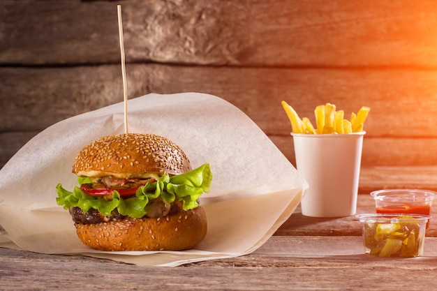 Hambúrguer em papel e batatas fritas Mesa com hambúrguer e batatas fritas Picles fatiados e fast food Almoço calórico no restaurante