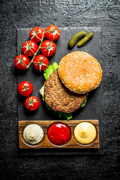Hambúrguer em uma placa de pedra com molhos e tomates em um galho
