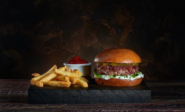 Foto hambúrguer fresco com batatas fritas na tábua de madeira escura e tigela de molho de tomate