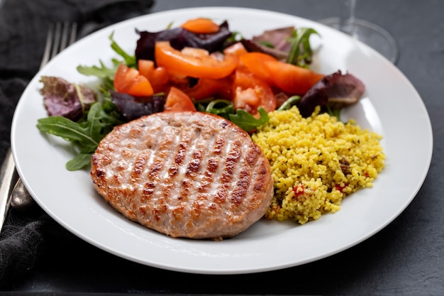 Hambúrguer grelhado com cereais e salada em prato branco sobre fundo de cerâmica