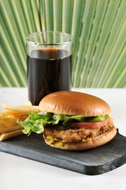 Hambúrguer redondo com costeleta de frango e batatas fritas e um copo de coca-cola