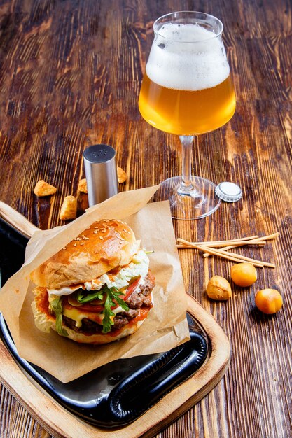 Hambúrguer saboroso com um copo de cerveja na mesa de madeira