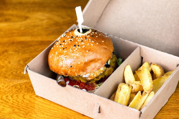 Hambúrguer saboroso fresco e batatas fritas em caixa de papel na mesa