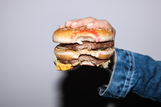 Hambúrguer segurando na mão sobre fundo cinza conceito de junk food no estilo de vida das pessoas