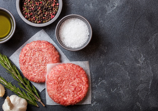 Hambúrgueres caseiros picados crus da carne da grade com especiarias e ervas. Vista do topo. Pimenta, sal e óleo na cozinha.