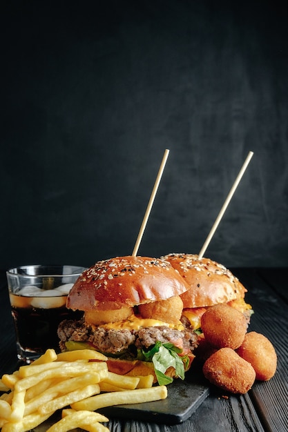 Hambúrgueres caseiros suculentos na placa de madeira, bolas de queijo. Comida de rua, comida rápida. com batatas fritas e um copo de coca-cola.