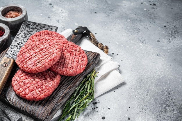 Hambúrgueres de carne de carne crua na placa de madeira de açougueiro com talhador de carne Fundo cinza Vista superior Copiar espaço