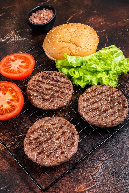 Foto hambúrgueres grelhados com tomate e temperos na mesa da cozinha fundo escuro vista superior