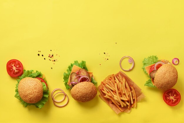 Hambúrgueres saborosos com carne, tomate, queijo, cebola, pepino e alface em fundo amarelo Espaço para cópia de vista superior Banner de fast-food Refeição para viagem Conceito de dieta pouco saudável