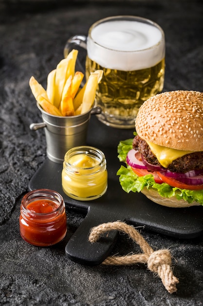 Hamburguesa de alto ángulo en la tabla de cortar con papas fritas, salsa y cerveza