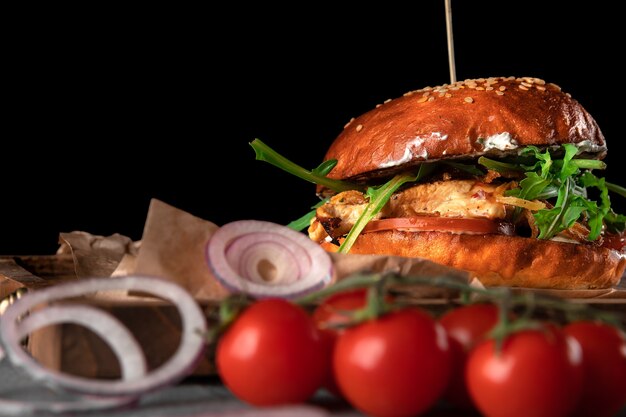 Hamburguesa americana grande sobre un fondo negro. chuleta con queso, tomate, pollo y rúcula en una bandeja de madera, espacio de copia, close-up