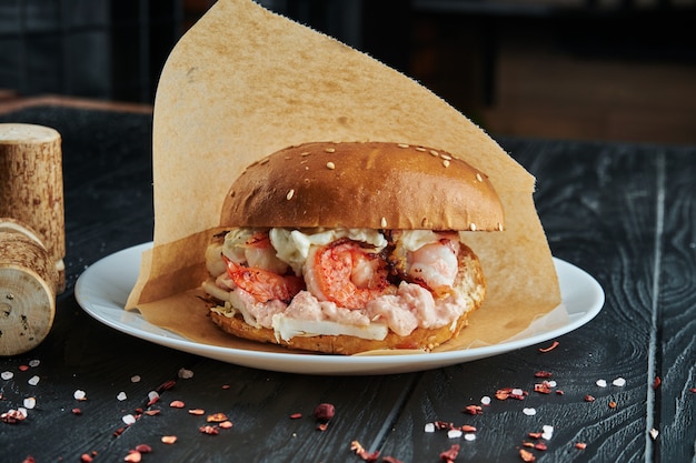 Hamburguesa apetitosa y jugosa con camarones, cebolla, salsa de caviar blanco en un plato blanco con papas fritas. De cerca