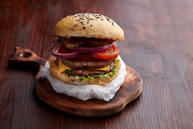 Hamburguesa apetitosa en el tablero sobre una mesa de madera oscura