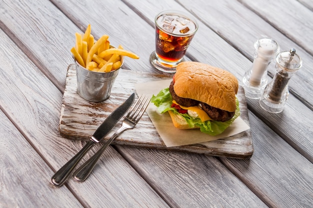 Hamburguesa y balde de patatas fritas. Vaso con cola. Delicioso refrigerio en el café americano. Bebida fría con sabor dulce.