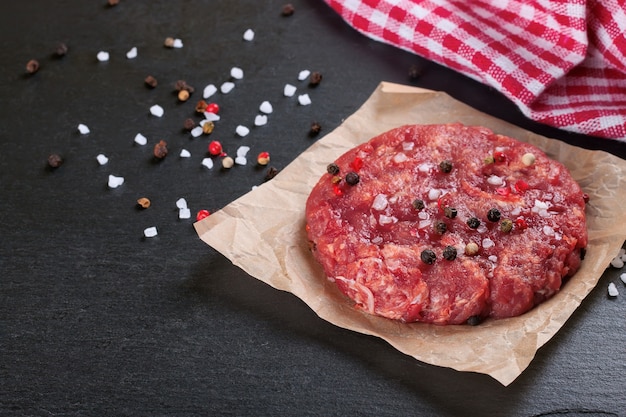 Hamburguesa de bistec de ternera picada casera fresca cruda con especias, sobre una mesa de pizarra negra, espacio de copia, vista superior