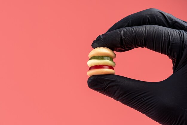 Hamburguesa de caramelo colorido con una mano en guante negro.