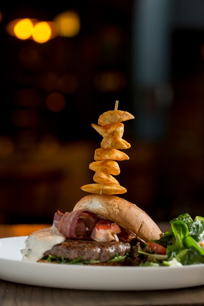 Foto hamburguesa de carne de res con queso chedar derretido, tocino, tomate, ensalada de rúcula con papas fritas picantes