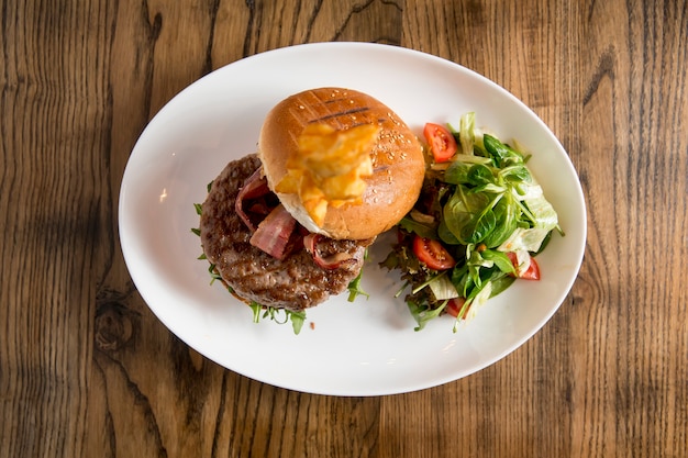 Hamburguesa de carne de res con queso chedar derretido, tocino, tomate, ensalada de rúcula con papas fritas picantes